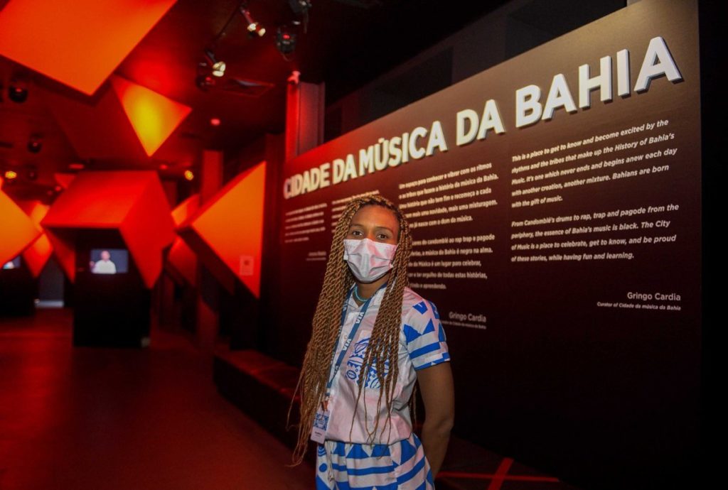 foto de mulher em frente a um painel escrito museu cidade da música da bahia
